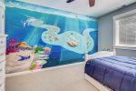 Downstairs bedroom with queen bed, twin bed trundle, and colorful mural at Moon Tide